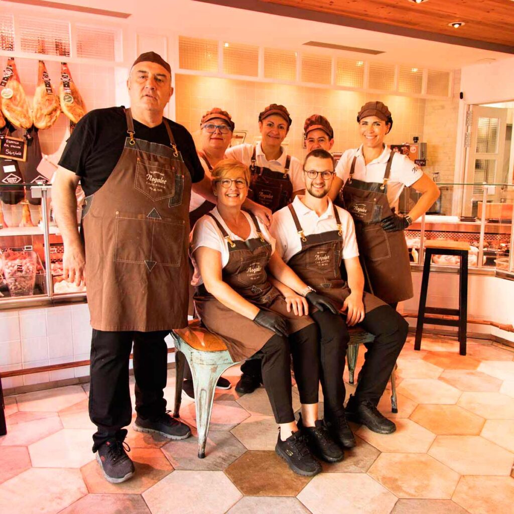 Fotografia on es veuen cinc dones i dos homes posant dintre d'una carnisseria amb la indumentària corporativa.