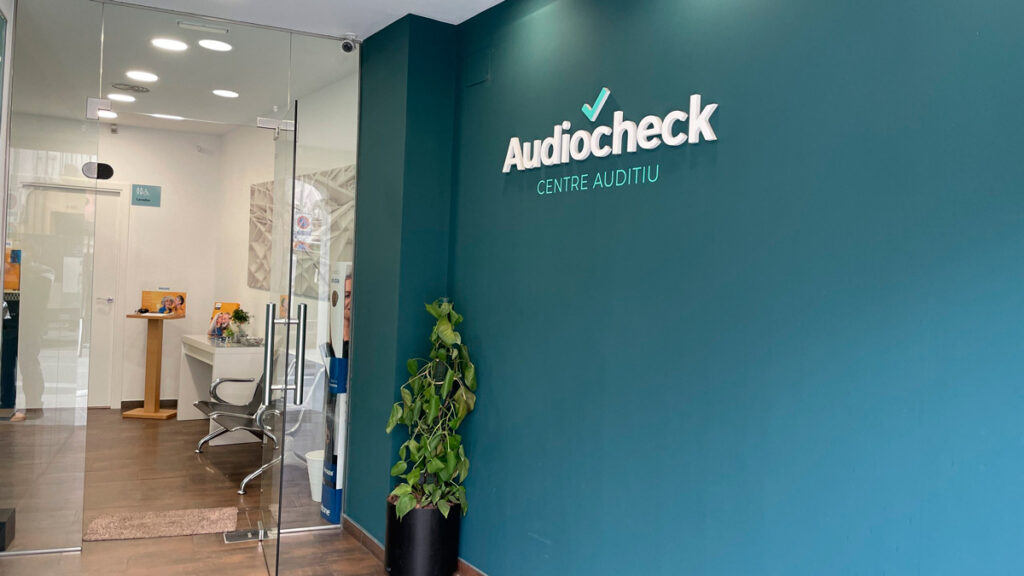 Entrada amb una paret pintada de color blau, on es veu el logotip Audiocheck, Centre Auditiu.