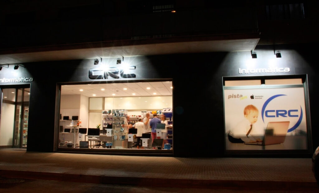 Fotografia feta durant la nit des de l'exterior, de l'aparador Informàtica CRC.